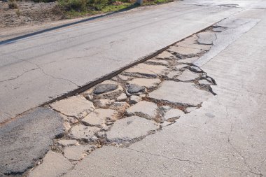 Damaged street with a large pothole and broken cracked surface, showing urban road infrastructure deterioration and the need for maintenance and repair.