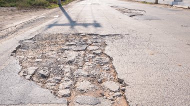 Büyük bir çukur ve kırık yüzey ile hasarlı asfalt yolu, kentsel altyapının bozulduğunu ve bakım ve onarım ihtiyacını gösteriyor..