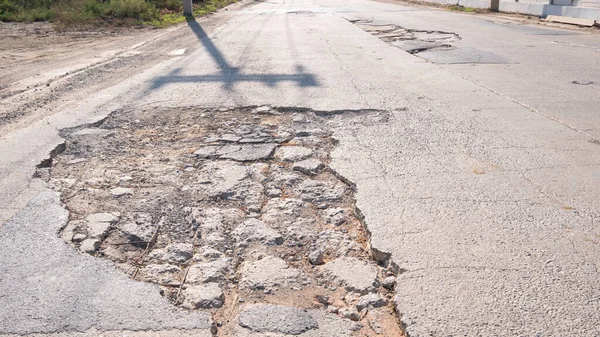 Büyük bir çukur ve kırık yüzey ile hasarlı asfalt yolu, kentsel altyapının bozulduğunu ve bakım ve onarım ihtiyacını gösteriyor..