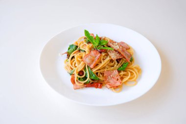 Pastırmayla kızartılmış baharatlı spagetti, kurutulmuş acı biber ve beyaz tabakta fesleğen. Tayland füzyon İtalyan yemeği tarzı. Beyaz arkaplanda izole