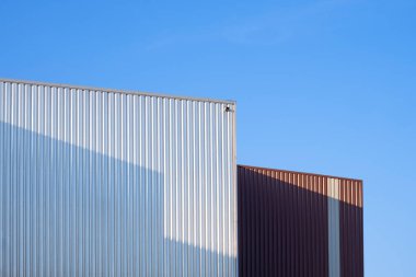 Açık mavi gökyüzüne karşı bükülmüş metal depo cephesinin minimalist mimari ayrıntıları, kopyalama alanı olan endüstriyel geometrik soyut arkaplan.