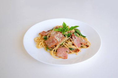 Pastırmalı spagetti ve beyaz tabakta kırmızı biber. Baharatlı otlu İtalyan makarnası, fesleğen sosu ve peynir. Menü tasarımı için nefis ev yapımı yemek fotoğrafçılığı.