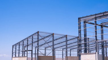 2 endüstriyel depo fabrika iskeletinin metal yapısı mavi gökyüzü arkaplanına karşı inşaat alanında, kopyalama alanı ile perspektif yan görünümü