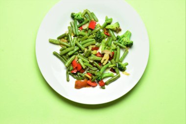 Yeşil arka planda beyaz dairesel bir tabakta çeşitli sebzelerin sunumu. Bir tabak iyi yiyecek, vitamin ve vücudumuz için sağlıklı..