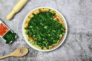 Ispanaklı pizza, pişirme aletleri ve gri taşın üzerindeki malzemeler. Zirve görünümü.