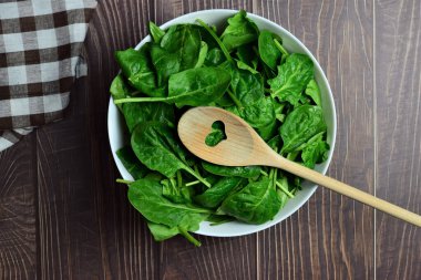 Beyaz kasede taze ıspanak yaprakları. Rustik tahta tahtalar ve kopyalama alanı.