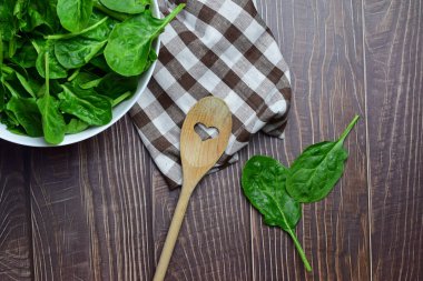 Zenith manzarası. Sağlıklı yiyecekler, ıspanak yaprakları, beyaz bir kâse ve kareli bir kumaş üzerinde, tahta kaşık..