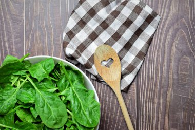 Zenith manzarası. Sağlıklı yiyecekler, ıspanak yaprakları, beyaz bir kâse ve kareli bir kumaş üzerinde, tahta kaşık..