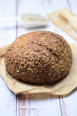 Çok tahıllı ekmek, açık renkli bir kırsal masada kese kağıdının üzerinde. Boşluğu kopyala..