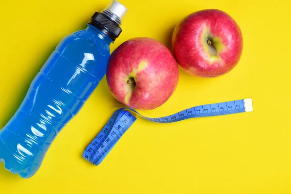 Apples and a bottle of isotonic drink, together with a measuring tape. Concept, eat healthy, play sports and keep the line. Yellow background and copy space.