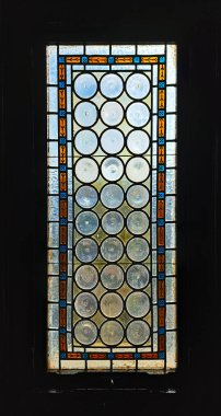 Güneş ışığıyla aydınlatılan turuncu, mavi ve siyah geometrik desenlerden oluşan renkli bir çerçeveyle çerçevelenmiş dairesel desenli cam camlı eski bir kilise penceresinin yakın çekimi.