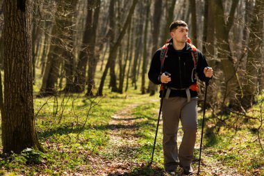 Erkek yürüyüşçü ormanda yürürken yan tarafa bakıyor.