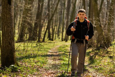 Erkek yürüyüşçü ormanda yürürken yan tarafa bakıyor.