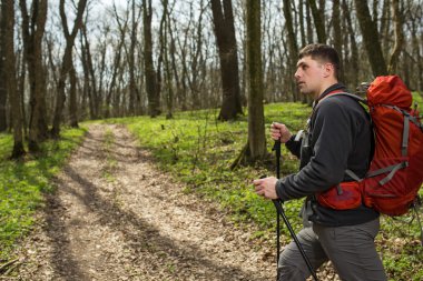 Erkek yürüyüşçü ormanda yürürken yan tarafa bakıyor.