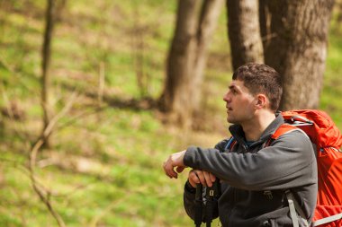Erkek yürüyüşçü ormanda yürürken yan tarafa bakıyor.