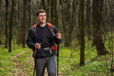 Erkek yürüyüşçü ormanda yürürken yan tarafa bakıyor.