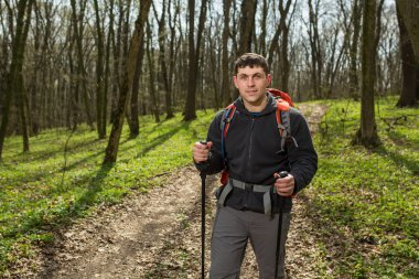 Erkek yürüyüşçü ormanda yürürken yan tarafa bakıyor.