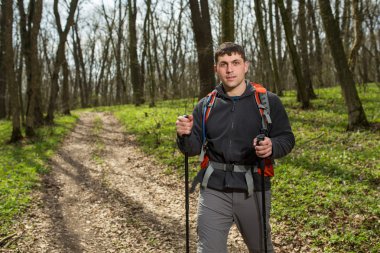 Erkek yürüyüşçü ormanda yürürken yan tarafa bakıyor.