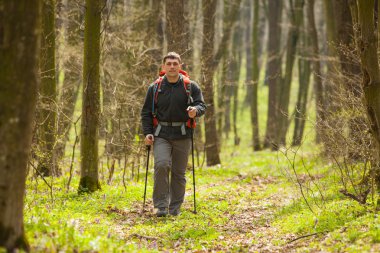 Erkek yürüyüşçü ormanda yürürken yan tarafa bakıyor.