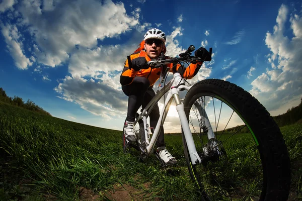 Motociclista em jersey laranja montando no campo de verão verde — Fotografia de Stock