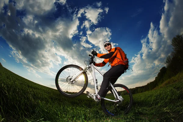 Rowerzysta w pomarańczowy jersey jazda na pole zielone lato — Zdjęcie stockowe