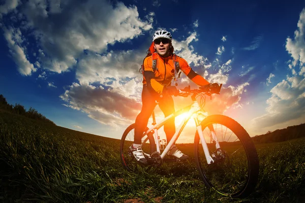 Motociclista em jersey laranja montando no campo de verão verde — Fotografia de Stock