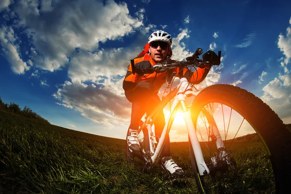 Motociclista em jersey laranja montando no campo de verão verde — Fotografia de Stock
