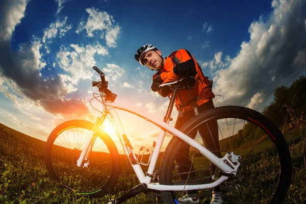 Rowerzysta w pomarańczowy jersey jazda na pole zielone lato — Zdjęcie stockowe