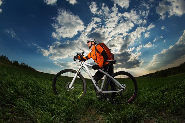 Rowerzysta w pomarańczowy jersey jazda na pole zielone lato — Zdjęcie stockowe