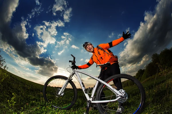 Ποδηλάτης πορτοκαλί φανέλα ιππασία στο πεδίο πράσινο καλοκαίρι — Φωτογραφία Αρχείου