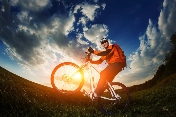 Rowerzysta w pomarańczowy jersey jazda na pole zielone lato — Zdjęcie stockowe