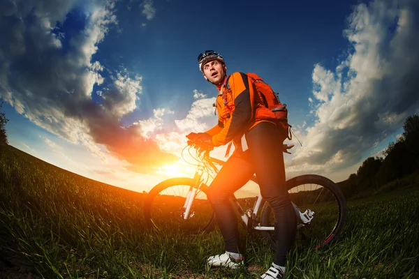 Biker in oranje trui rijden op groene zomer veld — Stockfoto