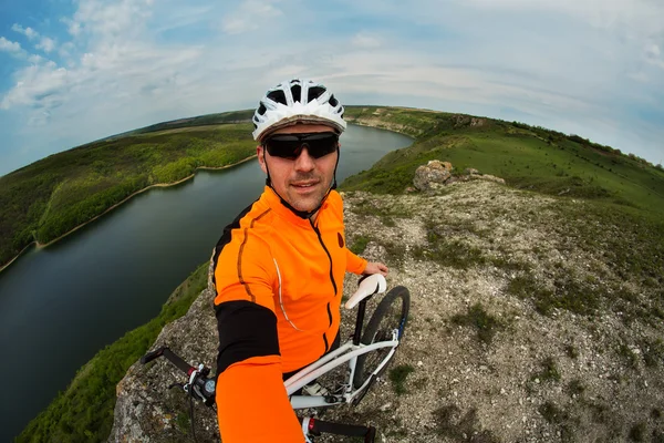 Fietser in oranje dragen met de fiets boven rivier — Stockfoto