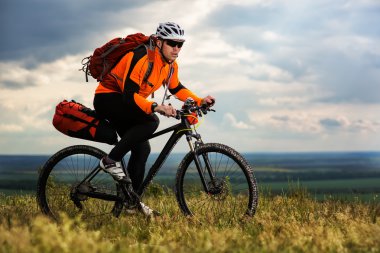 Genç adam yeşil çayır kırsal bir yolda Bisiklete binme