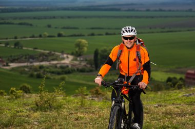 Genç adam yeşil çayır kırsal bir yolda Bisiklete binme