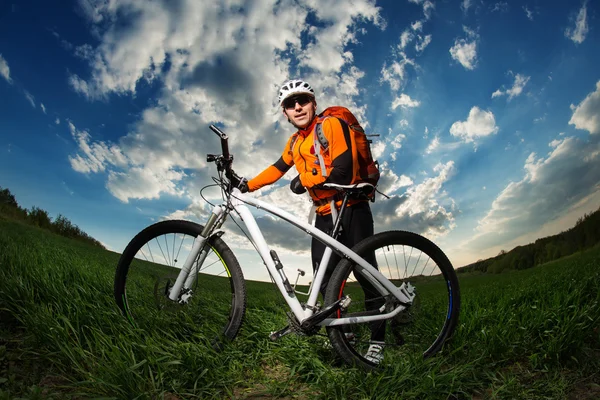 Biker in oranje trui rijden op groene zomer veld — Stockfoto