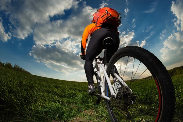 Rowerzysta w pomarańczowy jersey jazda na pole zielone lato — Zdjęcie stockowe