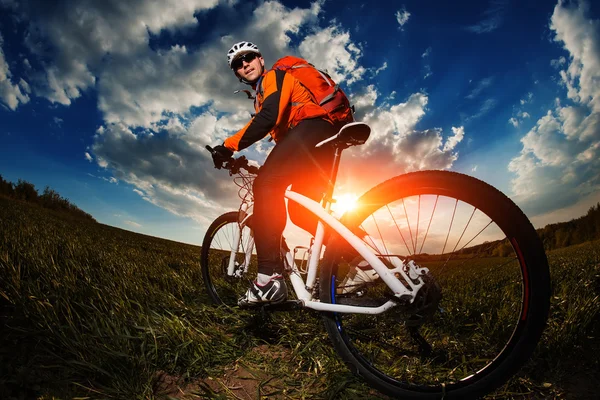 Rowerzysta w pomarańczowy jersey jazda na pole zielone lato — Zdjęcie stockowe