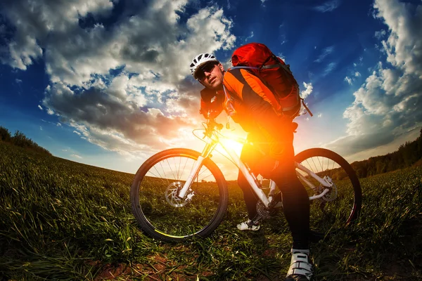 Biker im orangefarbenen Trikot auf grünem Sommerfeld unterwegs — Stockfoto