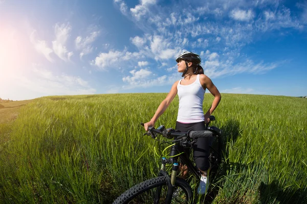 Vrolijke mooie jonge vrouw met fiets en helm op veld — Stockfoto