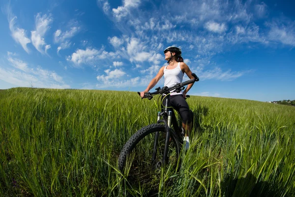 Vrolijke mooie jonge vrouw met fiets en helm op veld — Stockfoto