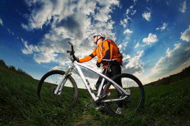 Genç adam sırt çantası ile derin çim ile bisiklet sürme
