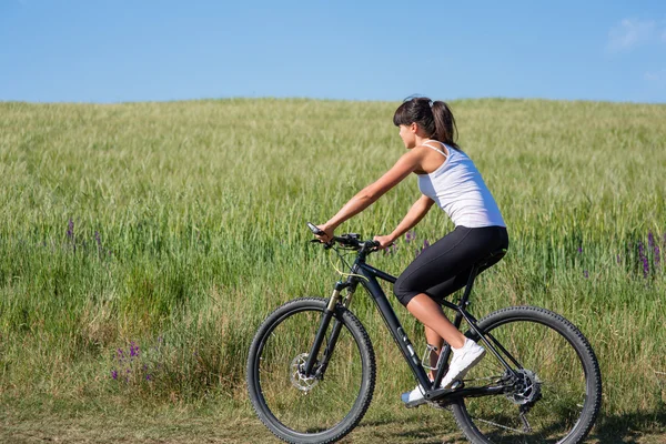 Спорт-велосипедна жінка на лузі з красивим пейзажем — стокове фото