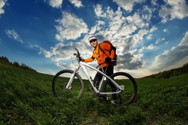 Joven montando en bicicleta a través de hierba profunda con mochila — Foto de Stock