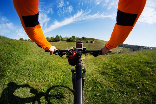Mãos na jaqueta cor-de-laranja que segura o guiador de uma bicicleta — Fotografia de Stock