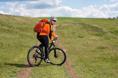 Genç adam yeşil çayır kırsal bir yolda Bisiklete binme