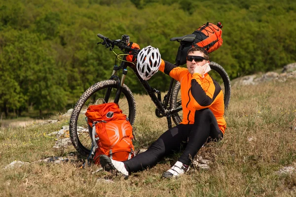 Joven ciclista en camisa naranja comprueba su teléfono — Foto de Stock