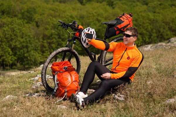 Mladý cyklista v oranžové tričko kontroluje jeho telefon — Stock fotografie