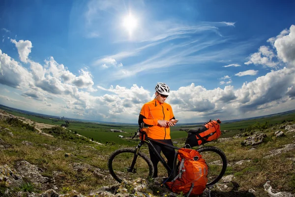 Junger Radfahrer im orangefarbenen Hemd checkt sein Handy — Stockfoto