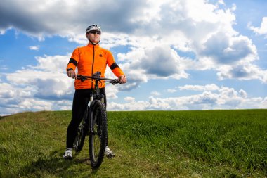 Genç adam yeşil çayır kırsal bir yolda Bisiklete binme